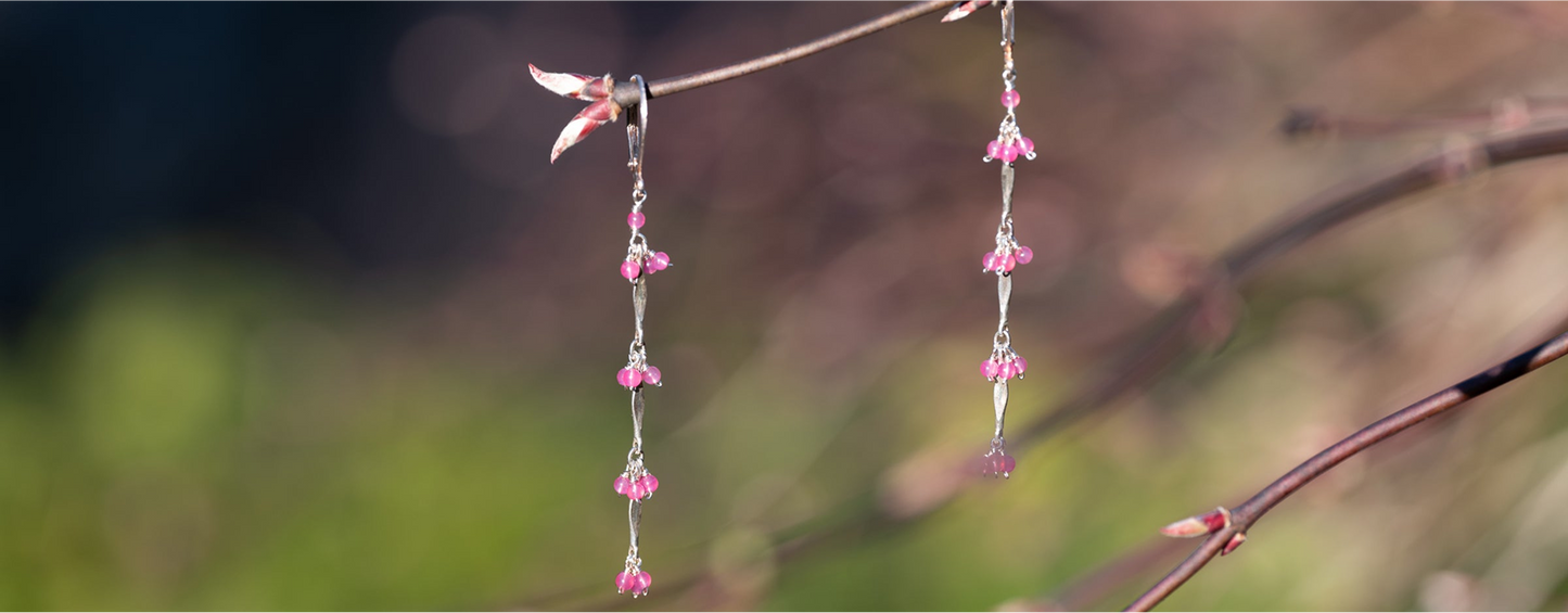 Pink beaded earrings hanging from a branch with a blurred natural background